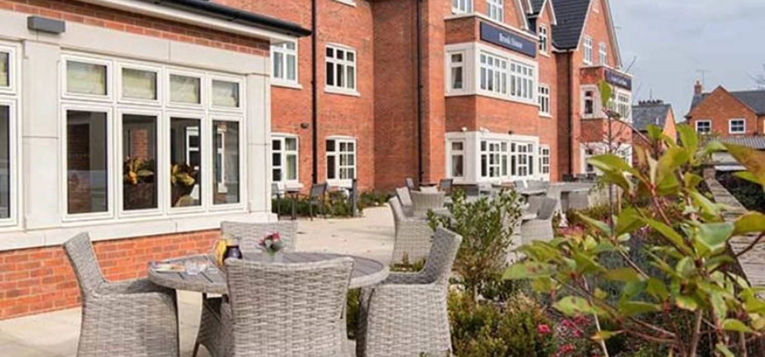 Exterior of Brook House care home, showing dining tables in a well-kept garden