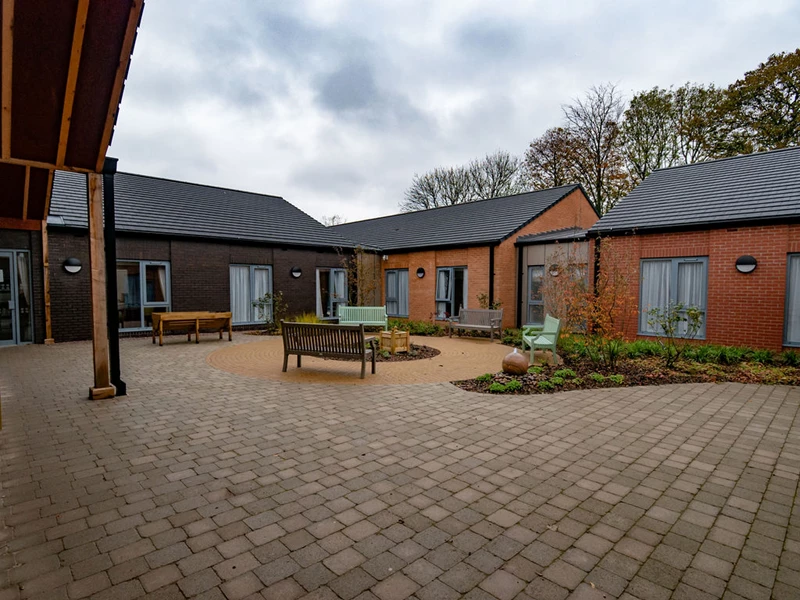 Courtyard of a care home with benches, plots of garden and trees in the background